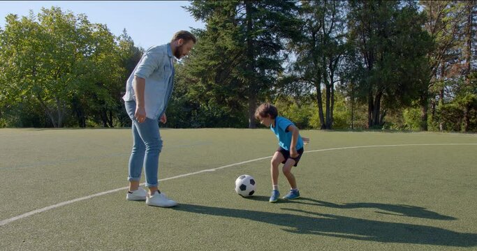 Young father and his little son tie their shoes and prepare to play soccer football on a green football pitch, 4k