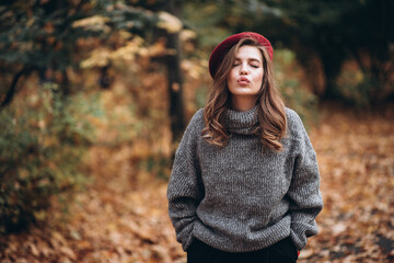 Fototapeta na wymiar Portrait of a joyful young woman enjoying in the autumn park. beautiful blonde girl in autumn red beret and gray sweater. Relax in nature