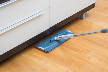 Housekeeper wiping wooden floor with mop under the cabinet
