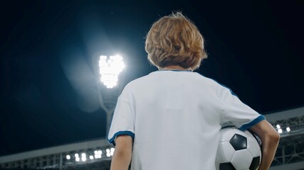 Portarit of Caucasian pre teen kid boy entering the field of huge soccer stadium, holding a ball, dreaming of becoming professional player, soccer star
