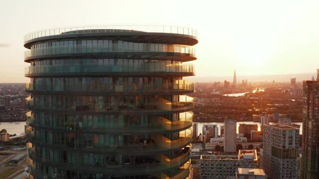 Pull back footage of futuristic cylindrical apartment building Arena Tower and skyline against sunset sky in background. London, UK