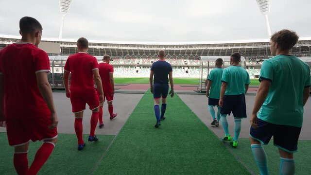 Professional football players goes to the Olympic stadium, rival football teams walk through the stadium, back view, football match.