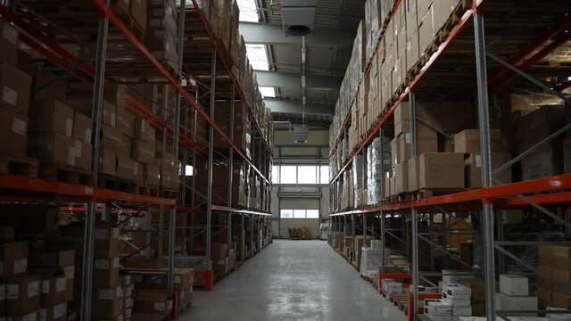 Warehouse indoors, aisle between racks on sides, shelves with pallets full of goods in cardboard boxes ready for delivery. Storehouse from inside, racks with products for shipment to customers