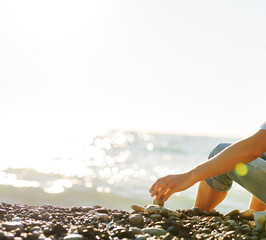 The hand of a man folding pebbles into a pyramid on the seashore.