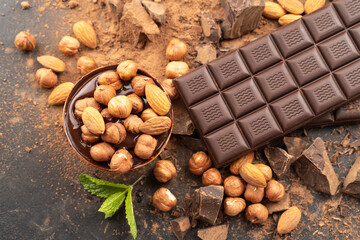 chocolate bar with hazelnuts, mint leaf, handmade sweets. Composition of bars dark chocolates hazelnuts, mint leaves on black background, top view. Pastry craft on the table for chocolate background