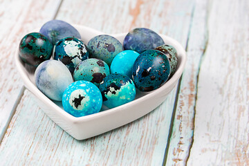 Easter blue quail eggs in a plate in the shape of a heart on a wooden table