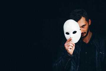 Handsome Strong Man Hides Behind a Mask in the Dark Background
