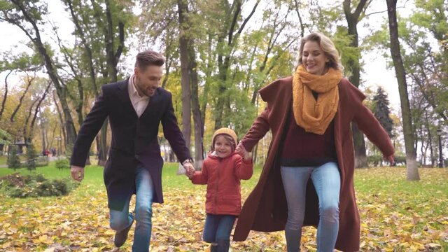 Loving couple with child walks in the autumn park, holding hands. Outdoor shot of a young family running on the lawn through the autumn park. Tinted image. High quality FullHD video.