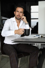 Poranna prasa i praca podczas pierwszej kawy. Przystojny mężczyzna w białej koszuli pije...