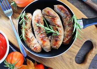 Grilled sausages on pan with herbs and spices, wood background, closeup