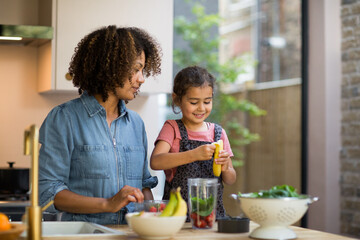 Mixed race girl making a smoothie with mother in kitchen