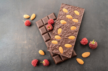 assortment chocolate bars with almonds, raspberries, handmade sweets. Composition of bars milk and dark almond chocolate, raspberries on a black background, top view. Pastry craft on the table