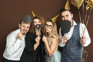 Happy people wearing party hats with photo booth props are celebrating holiday or event - obrazy, fototapety, plakaty