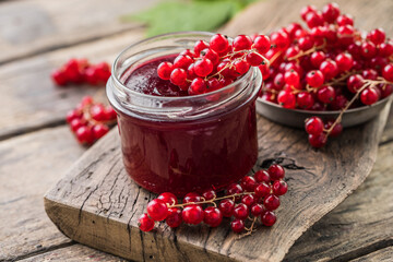 Red, juicy berries of red currants and jars of berry jam on a wooden table