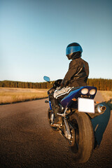 Motorcycle driver in helmet and leather jacket sits on sports motorcycle on the road against forest background. Beautiful background, a place for copy space
