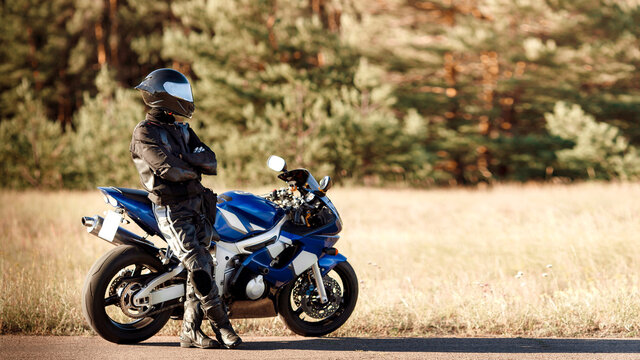 Motorcycle driver in helmet and leather jacket sits on sports motorcycle on the road against forest background. Beautiful background, a place for copy space