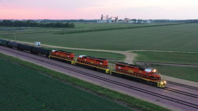 Aerial tracking shot of freight train slowing down as it drives across open fields in the evening