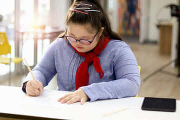 Portrait of girl with down syndrome concentrate on concentrate on study in classroom at school, kid...