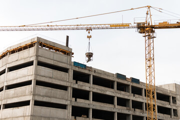 A construction tower crane lifts a concrete mixer to the roof of a building under construction....