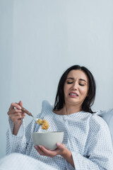 disgusted woman holding spoon with corn flakes and bowl in hospital