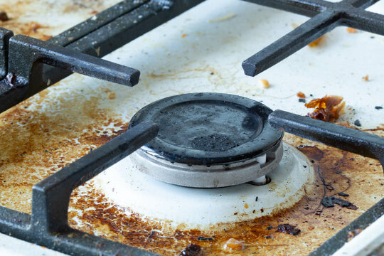 Dirty gas stove surface. Medium gas burner and cast iron grate of a gas oven surrounded by old leftovers of food and drinks. Top area surface and burner heads needs cleaning from burnt-on grease