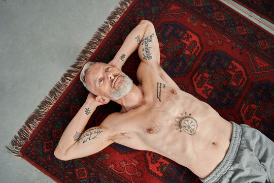 Naked man with tattoos laying at the floor after exercises and relaxing