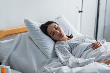 brunette woman in patient gown lying in hospital bed - obrazy, fototapety, plakaty
