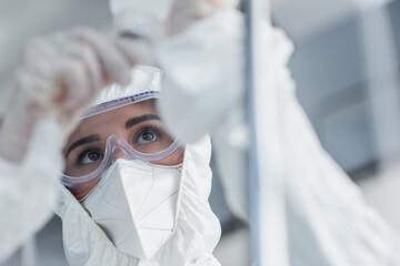 doctor in hazmat suit, medical mask and goggles holding catheter on drop counter