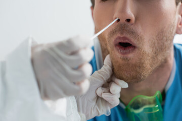 partial view of doctor in latex gloves holding swab near nose of curly patient while doing nasal pcr test