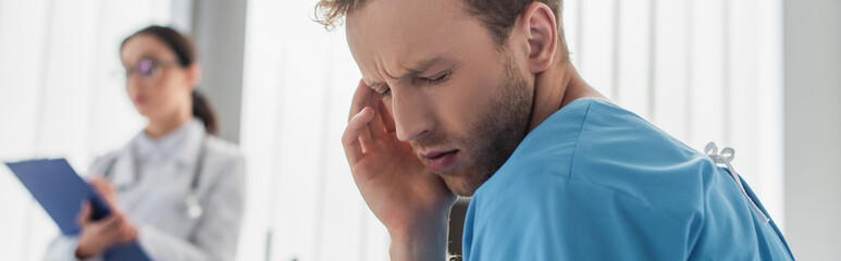 Obraz premium curly patient suffering from headache near blurred doctor in hospital, banner