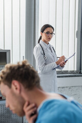 Fototapeta premium brunette doctor looking at blurred patient suffering from sore throat in hospital