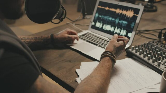 Close up with slowmo of hands of unrecognizable man with tattoos sitting at table and talking into microphone while recording online radio show or podcast