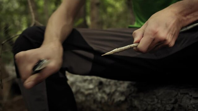 Hunter man with knife cut a wooden stick. Survivalist