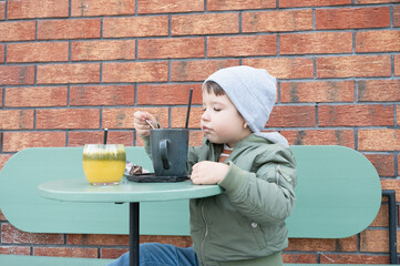 Little cute boy enjoys drinking cocoa in a cafe on the street