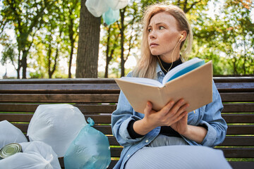 Shocked young female sitting at the bench and being afraid of amount of rubbish around