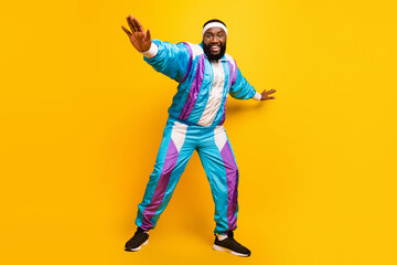 Photo of excited funny dark skin guy dressed sport suit headband smiling dancing isolated yellow...
