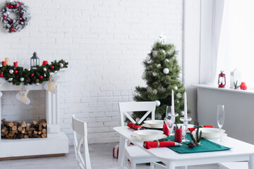 modern living room with decorated fireplace, christmas tree and table served for festive dinner