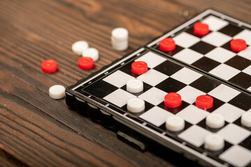 A board for playing checkers with chips on a wooden table, close-up, selective focus.