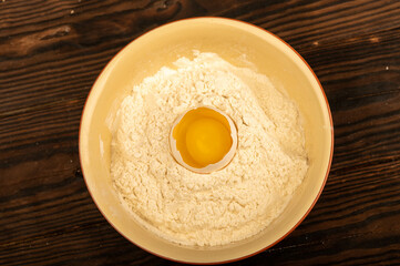 A broken white chicken egg in a bowl of wheat flour, close-up selective focus.