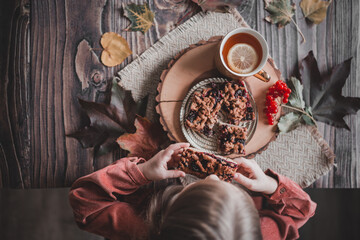 concept: autumn tea party, a girl eats a pie and drinks tea with lemon sitting at a wooden table,...