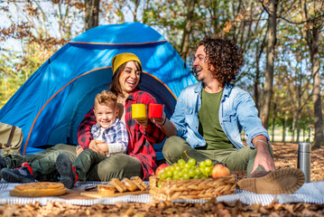 young happy family camping outdoor with tent in autumn nature. mom, dad and little child having a...