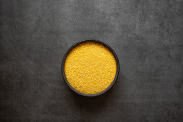 Yellow millet in spoon and bowl on dark grey background.