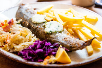 Fresh whole grilled trout served with french fries, red and white cabbage in ceramic plate