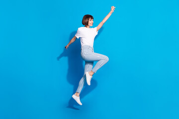 Fototapeta na wymiar Photo of adorable pretty young lady wear white outfit smiling walking rising fist looking empty space isolated blue color background