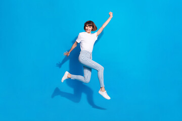 Fototapeta na wymiar Photo of shiny pretty young woman dressed casual clothes running rising fists smiling isolated blue color background