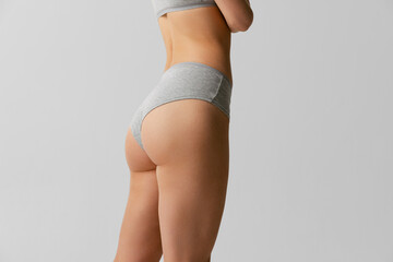 Back view of sportive body, bottocks of young woman in grey bottocks isolated on gray studio background. Natural beauty concept