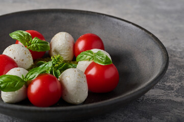 Macro panoramic view italian caprese salad with ripe tomatoes, fresh basil and mozzarella cheese in black plate. Selective focus
