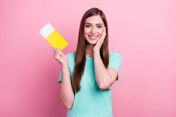 Photo of impressed excited young lady wear teal t-shirt smiling holding tickets arm cheek isolated pink color background