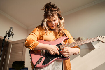 Woman songwriter playing guitar and singing lyrics song in front of the microphone