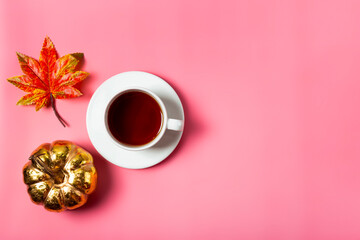  A cup of tea, autumn leave and golden pumpkin on the pink background top view. The concept of a cozy autumn at home with copy space for text.